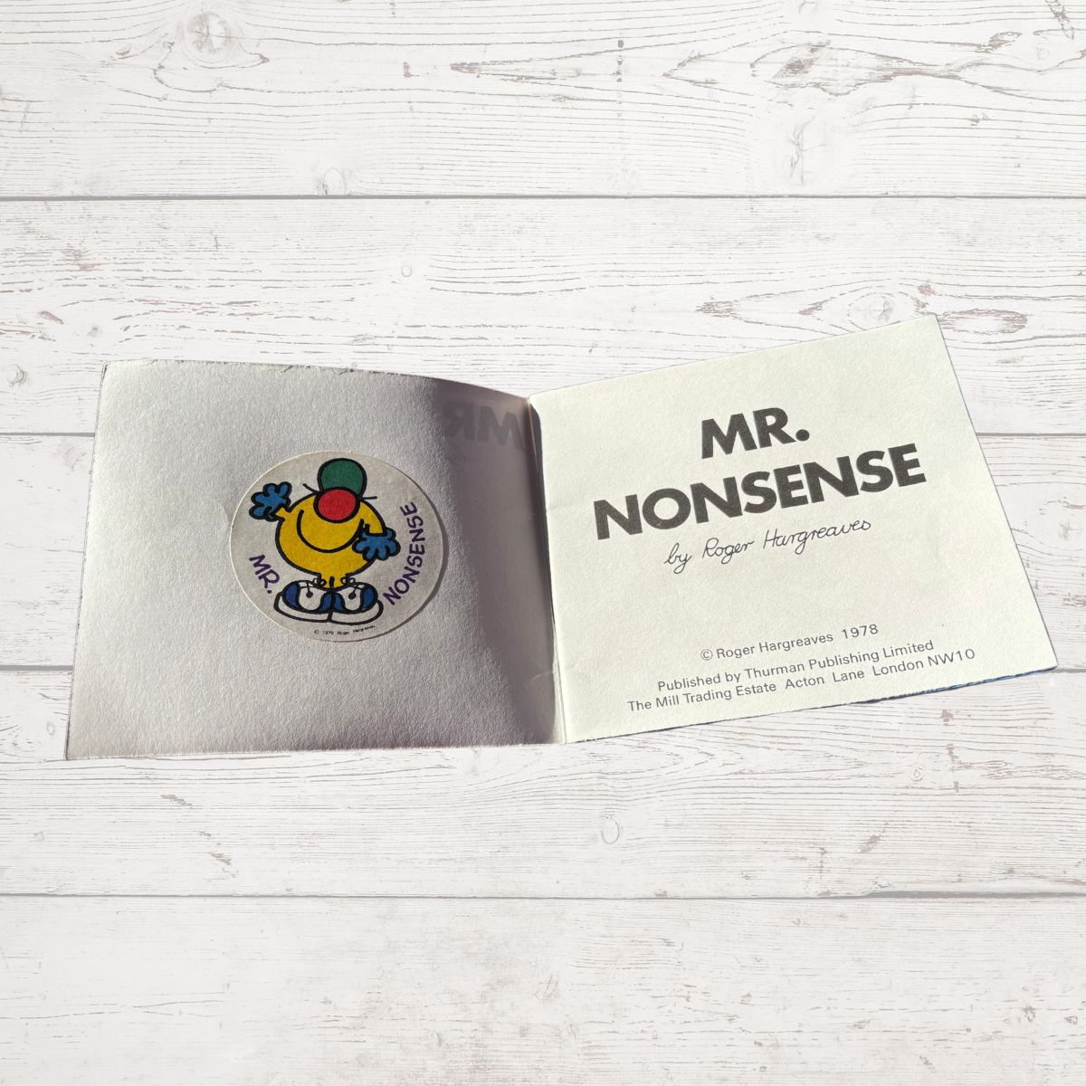 Open book with 'Mr. Nonsense' sticker and card on a light wooden surface