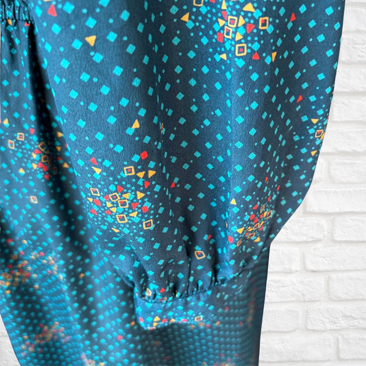 Blue dress sleeve with colorful geometric pattern on a white brick wall background