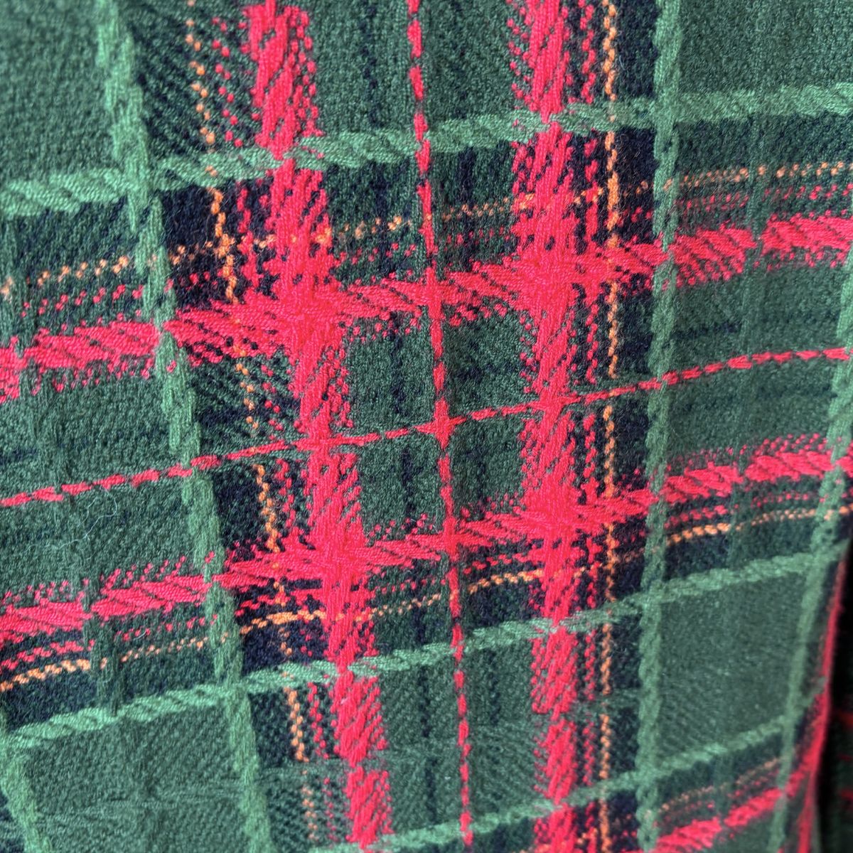 A close-up of a tartan plaid fabric pattern featuring dark green, vibrant red, and thin orange stripes.