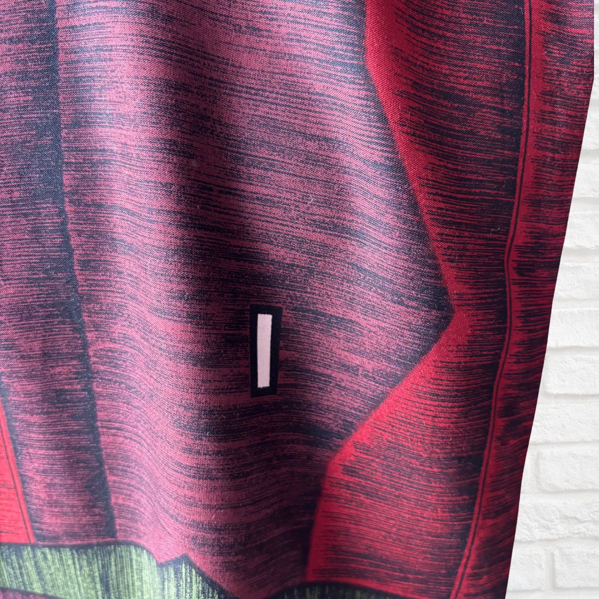 Close up of a red, burgundy and green scarf with black lines and white oblong