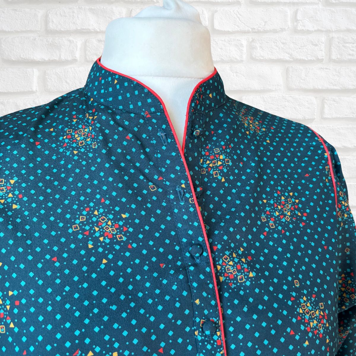 Mannequin wearing a blue patterned dress with red trim against a white brick wall.