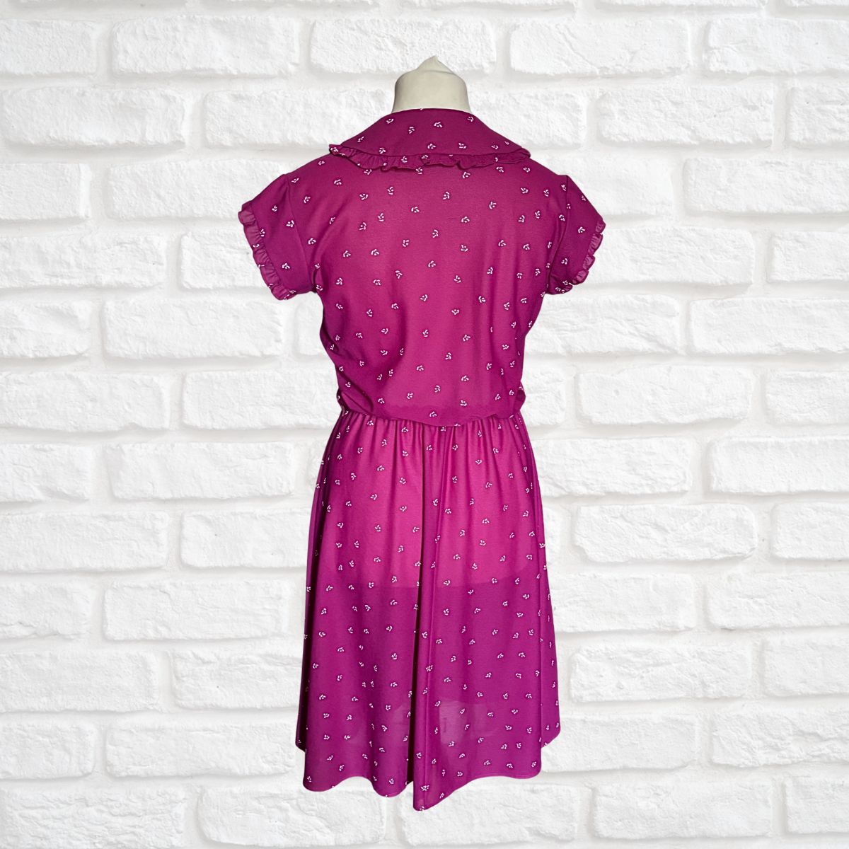 Pink dress with white patterns on a mannequin against a white brick wall background