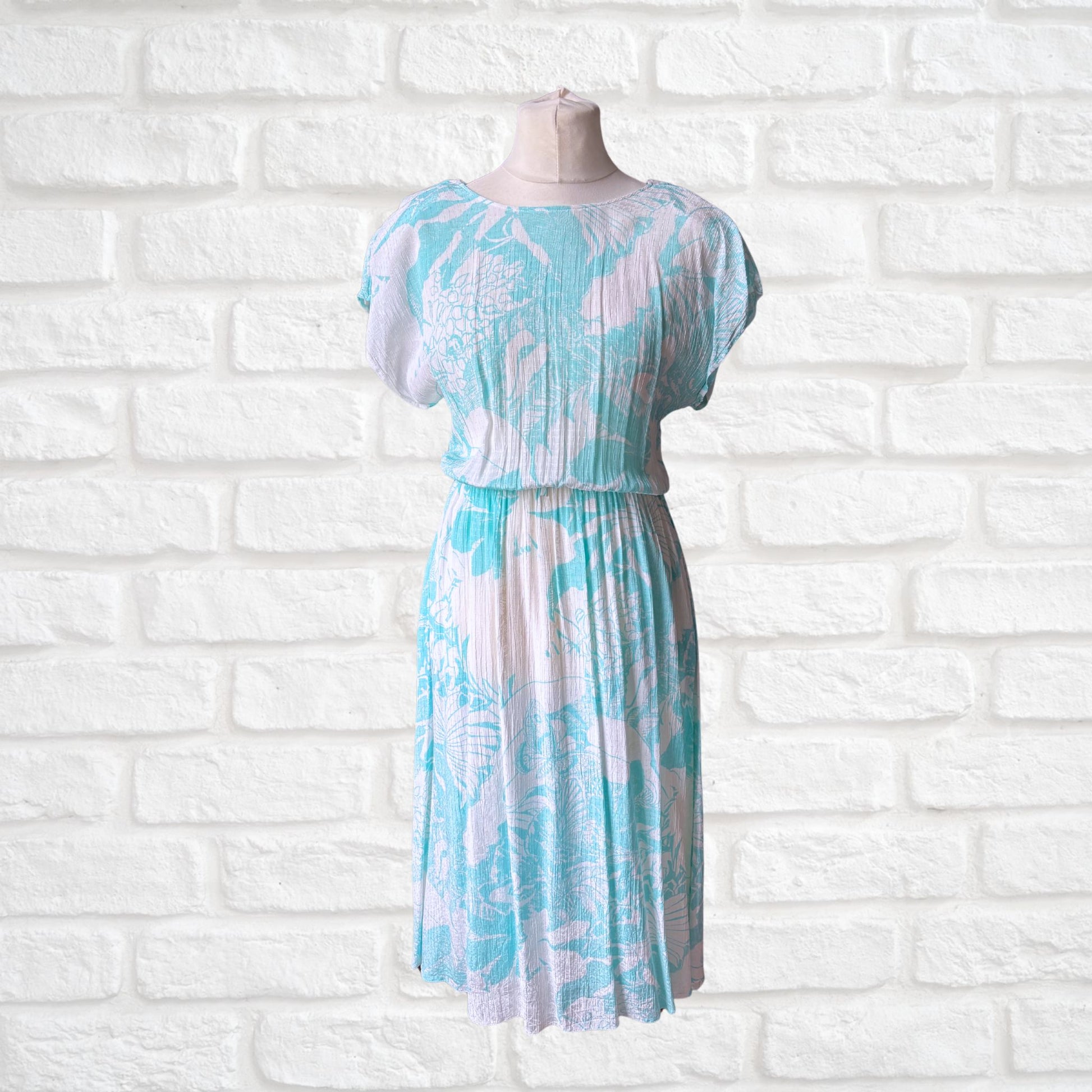 A vintage Betty Barclay midi dress featuring a white and turquoise floral print, displayed on a mannequin against a white brick wall background.