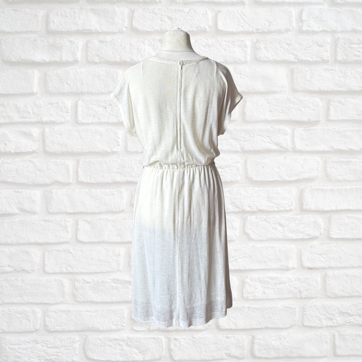 Cream dress on a mannequin against a white brick wall