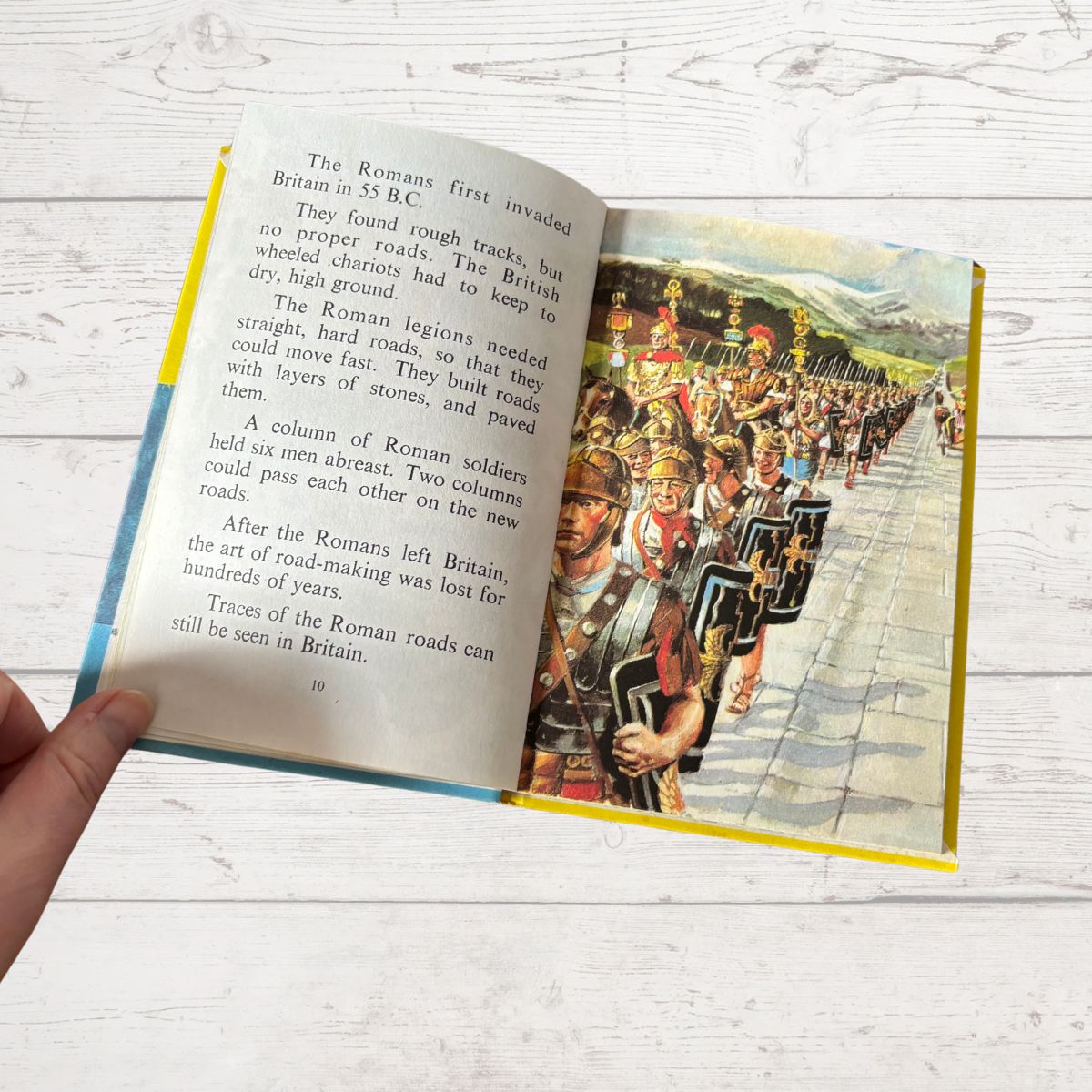 Open book showing a page with Roman soldiers on a road and text about Roman invasions.