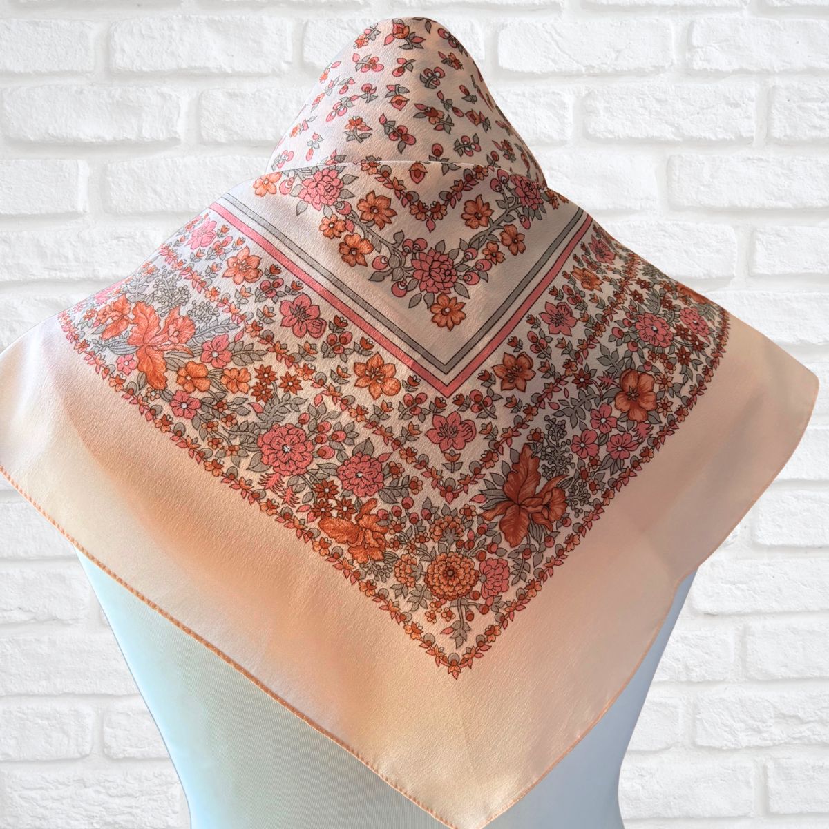 Floral patterned scarf on a mannequin against a white brick wall background