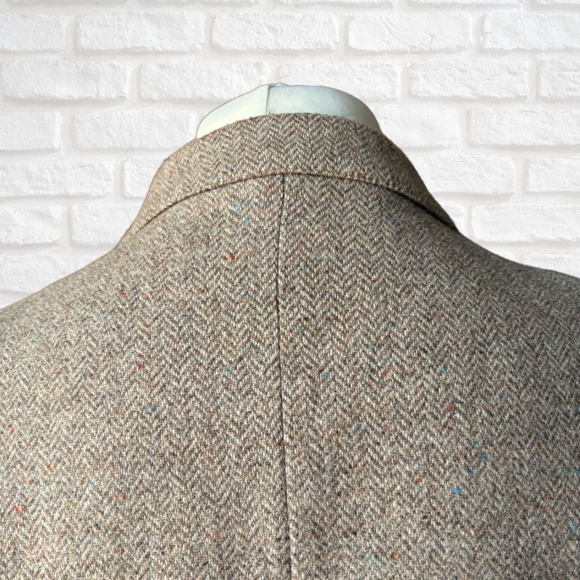herringbone patterned coat on a mannequin against a white brick wall background