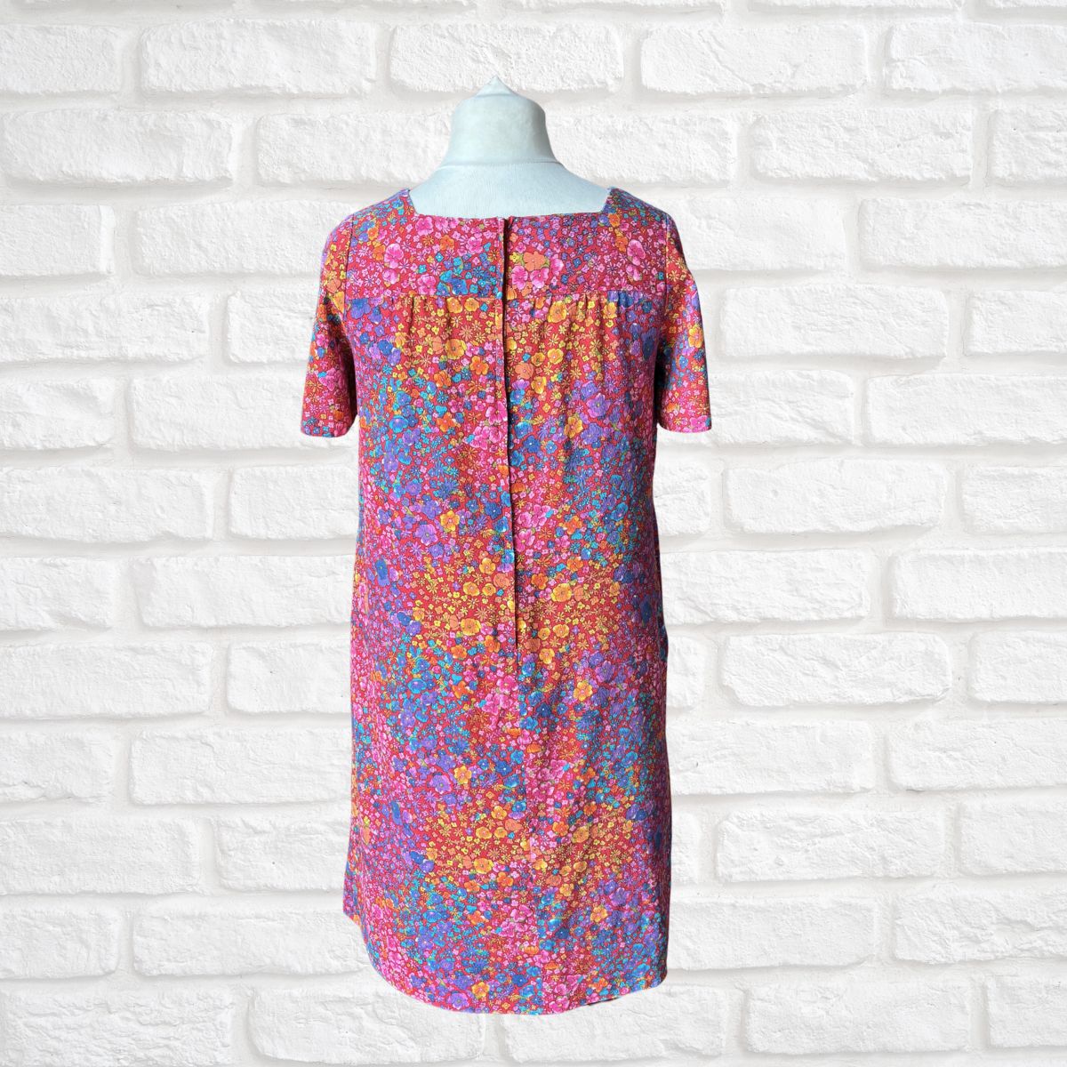Colorful floral dress on a mannequin against a white brick wall background