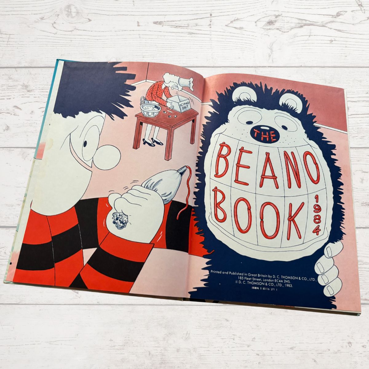 Open book showing illustrations of cartoon characters with 'The Beano Book' title on a wooden surface.