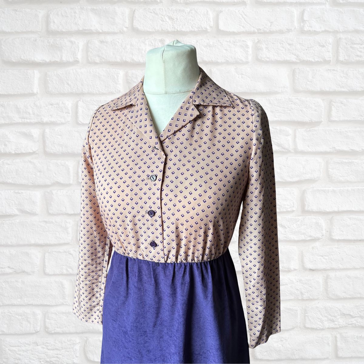 Mannequin wearing a patterned dress against  a white brick wall.