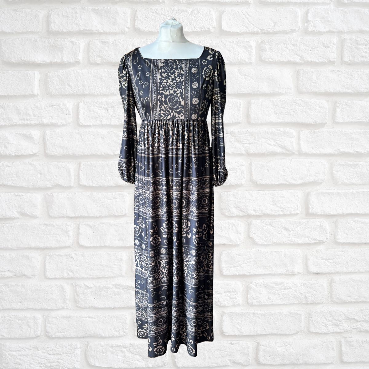 Black patterned dress on a mannequin against a white brick wall.