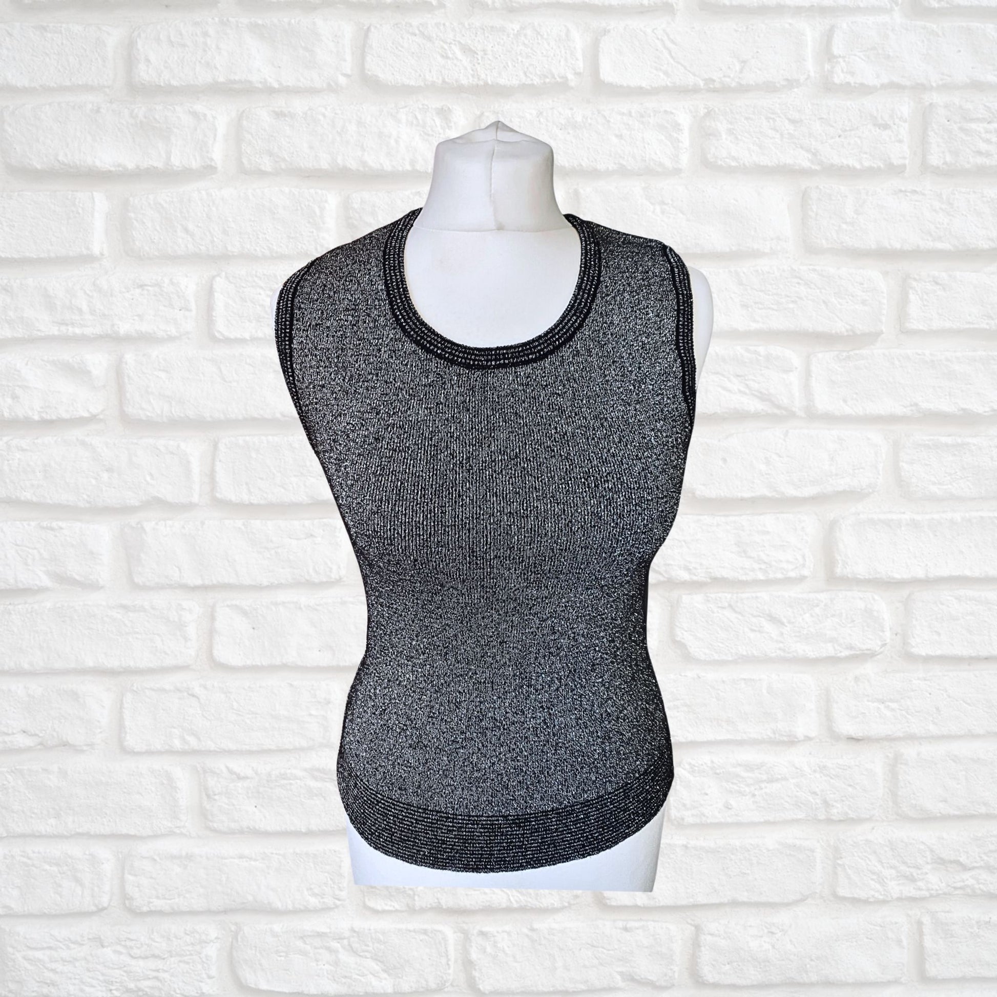 A sleeveless black and silver glittery tank top displayed on a mannequin, with striped detailing around the hem, armholes, and neckline.