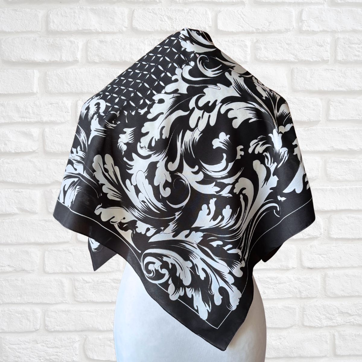 Black and white patterned scarf on a mannequin against a white brick wall background