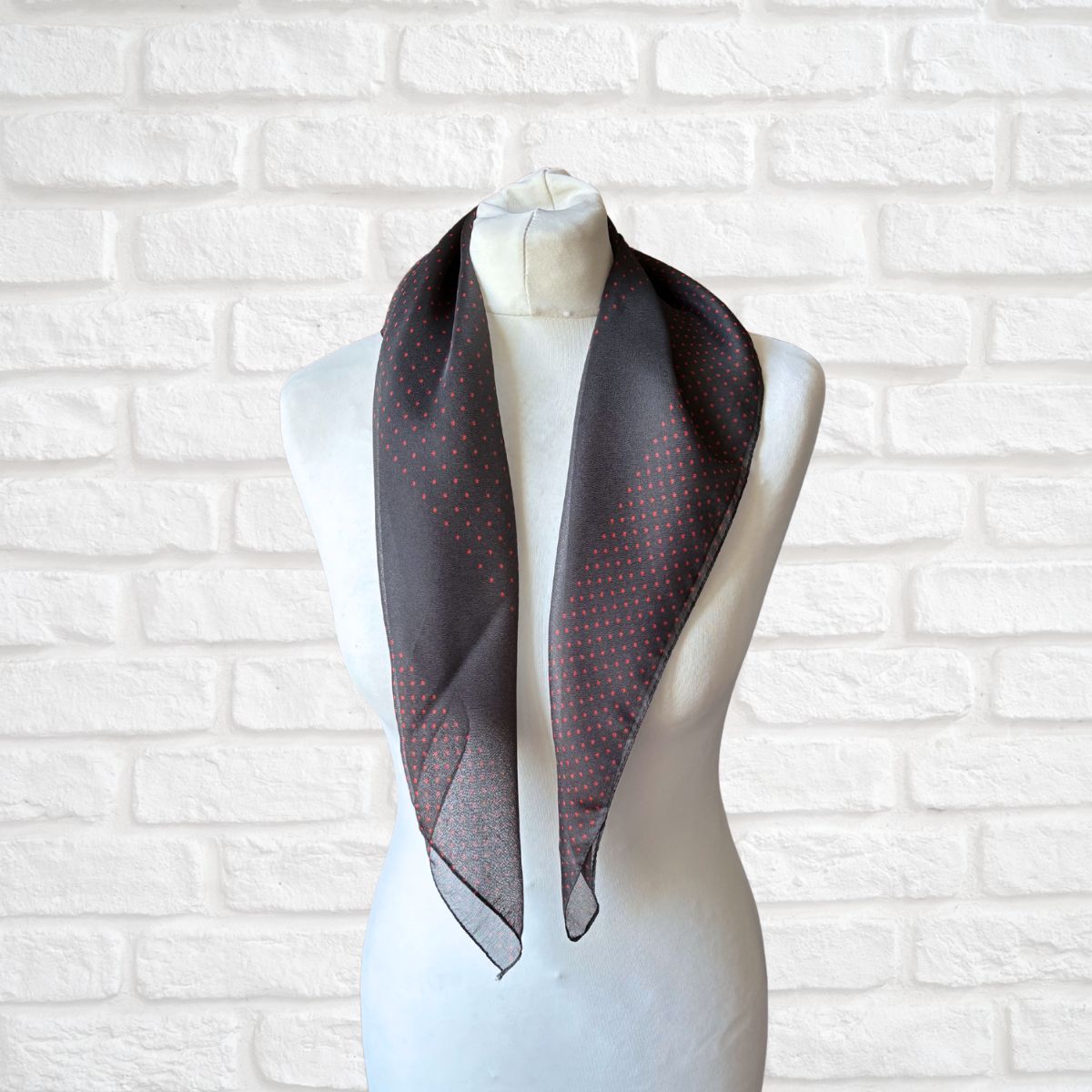 Mannequin wearing a dark gray scarf with subtle pattern against a white brick wall.
