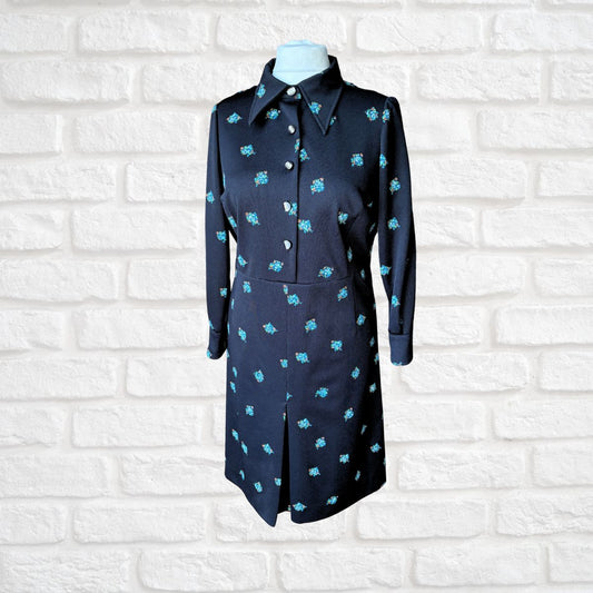 Black dress with turquoise patterns on a mannequin against a white brick wall.