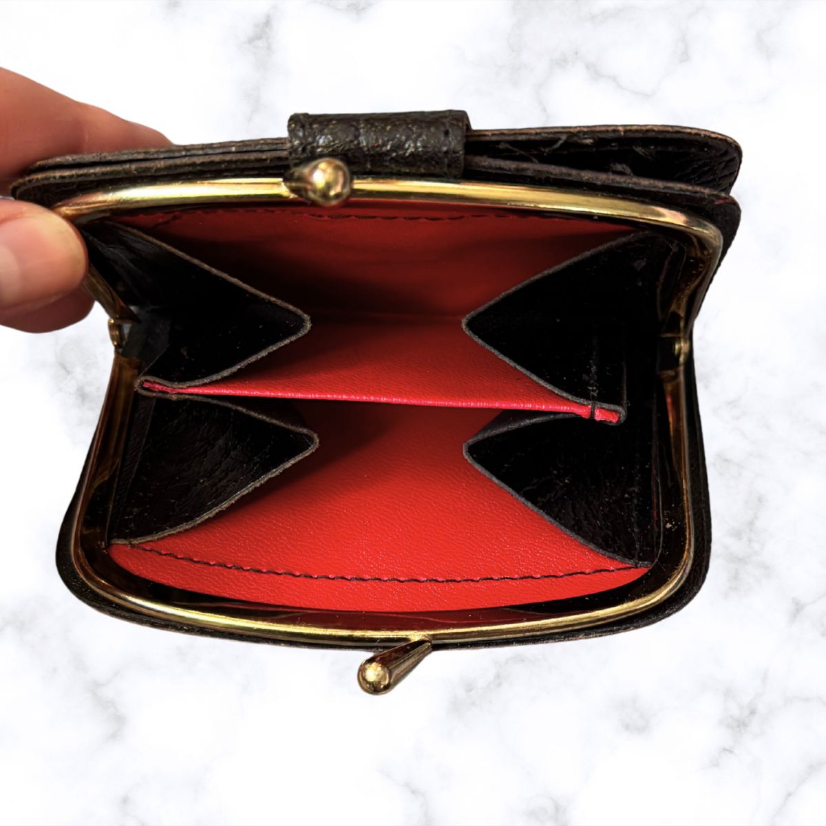 Small open wallet with red interior and gold trim held by a hand on a white background