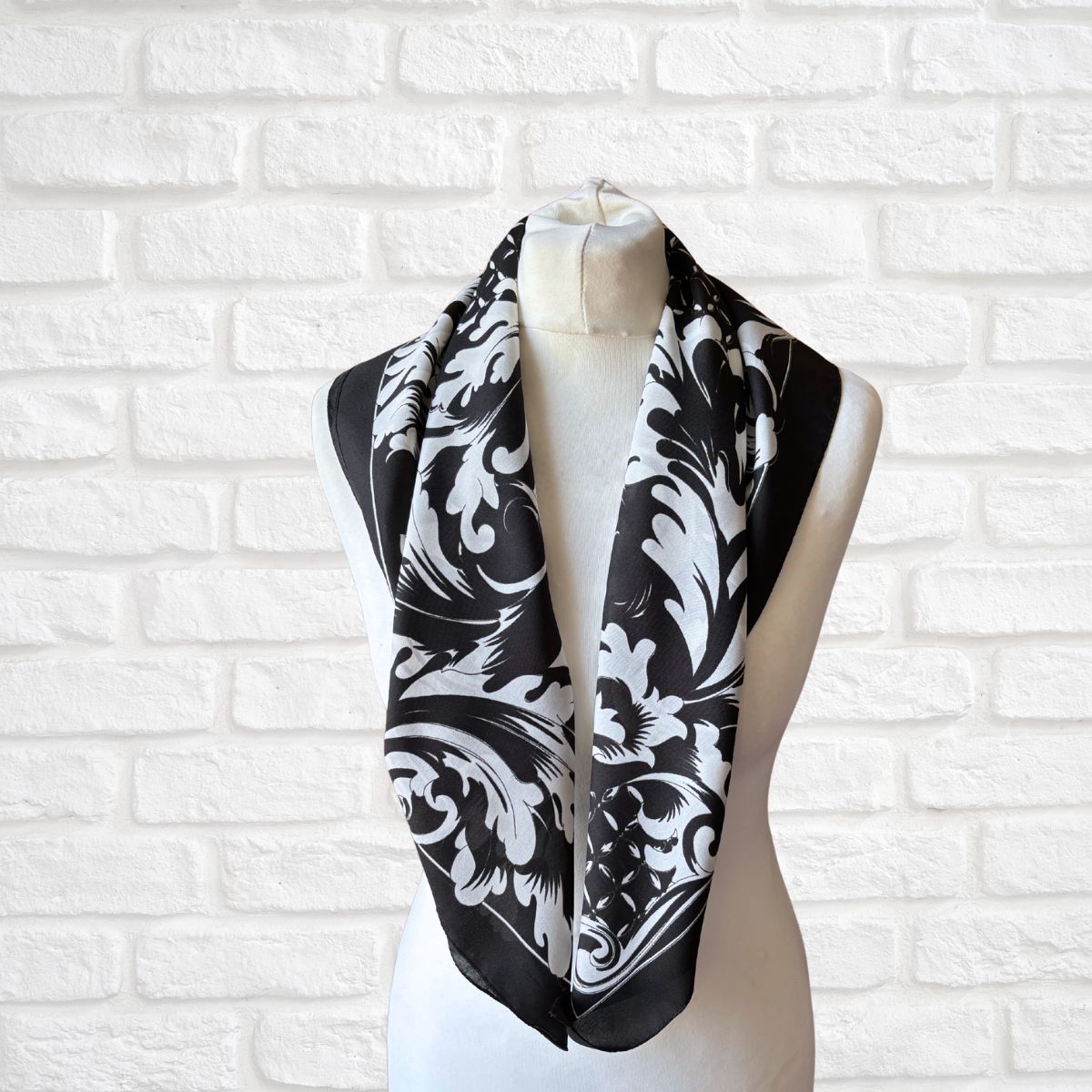 Black and white patterned scarf on a mannequin against a white brick wall.
