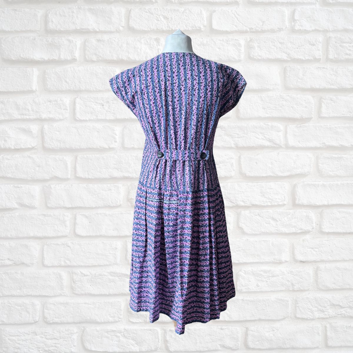 Purple patterned dress on a mannequin against a white brick wall background