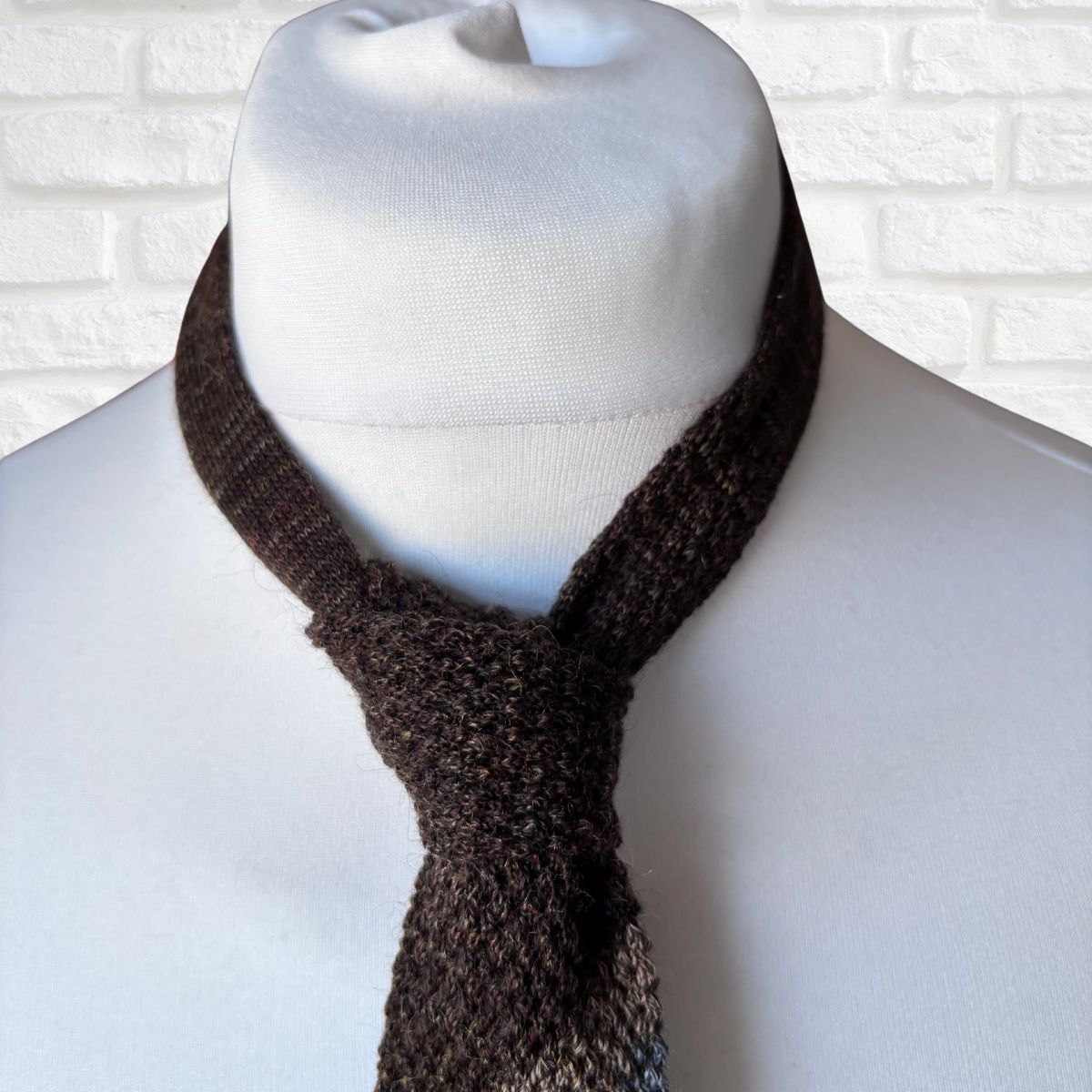 Mannequin wearing knitted skinny tie against a white brick wall.