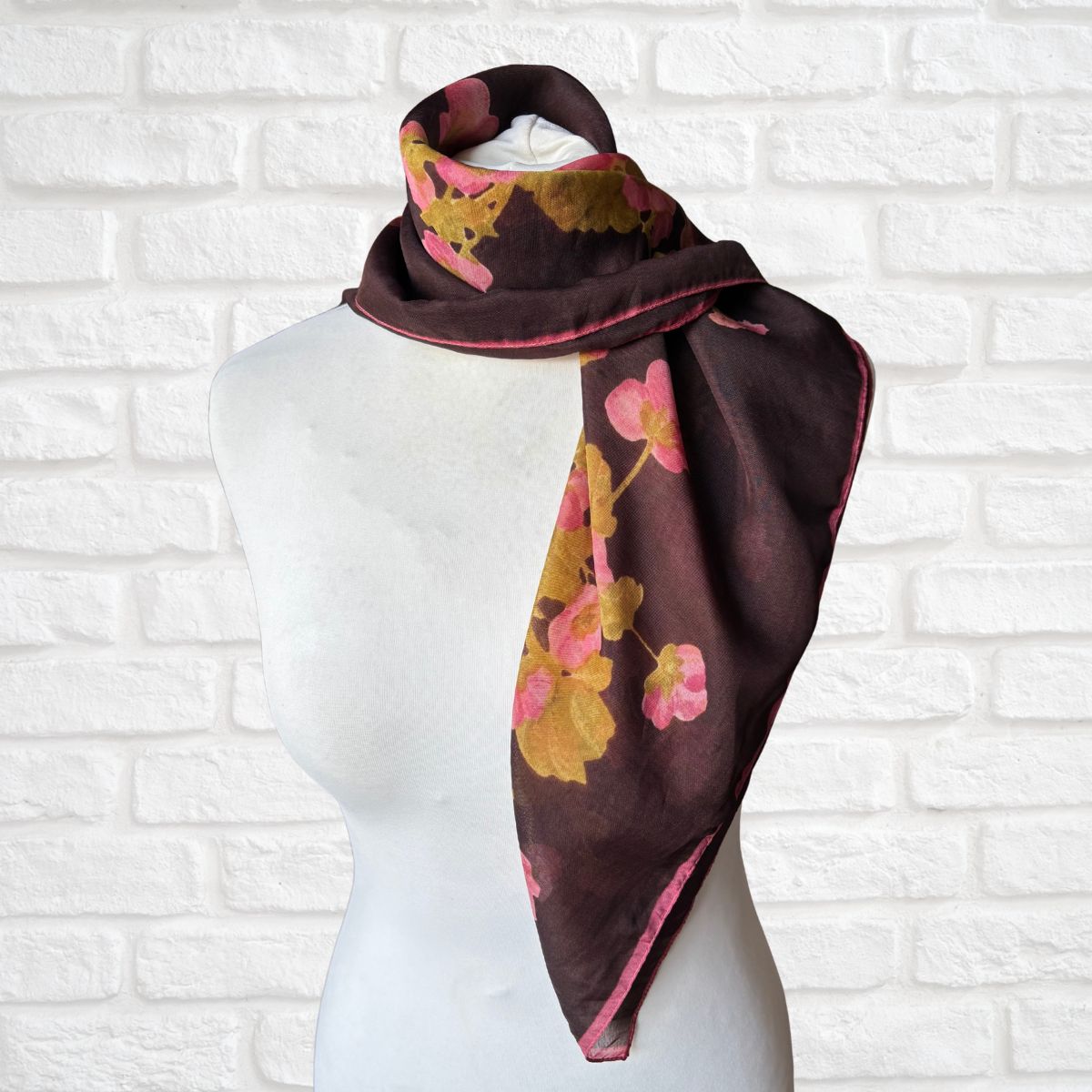 Floral patterned scarf on a mannequin against a white brick wall background