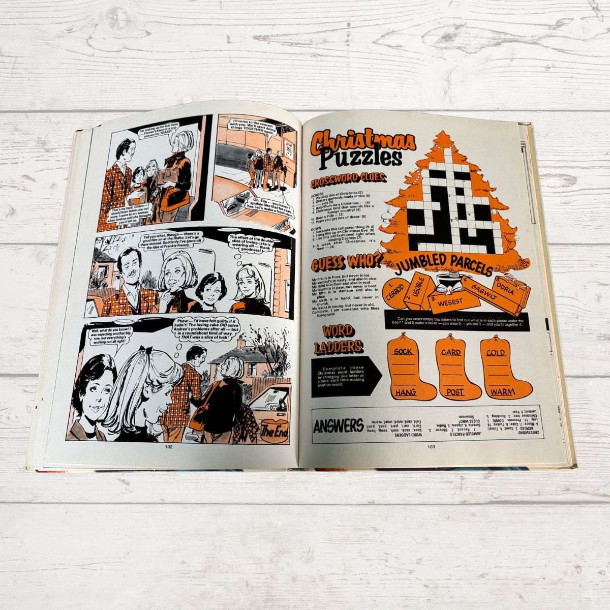Open book with comic strip and Christmas puzzle on a wooden surface