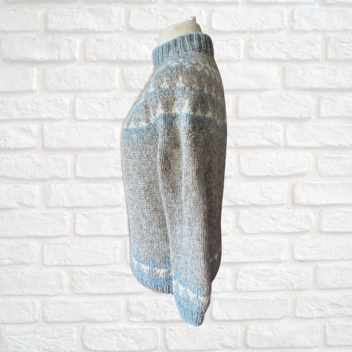 Knitted grey, white and blue jumper on a white brick wall background