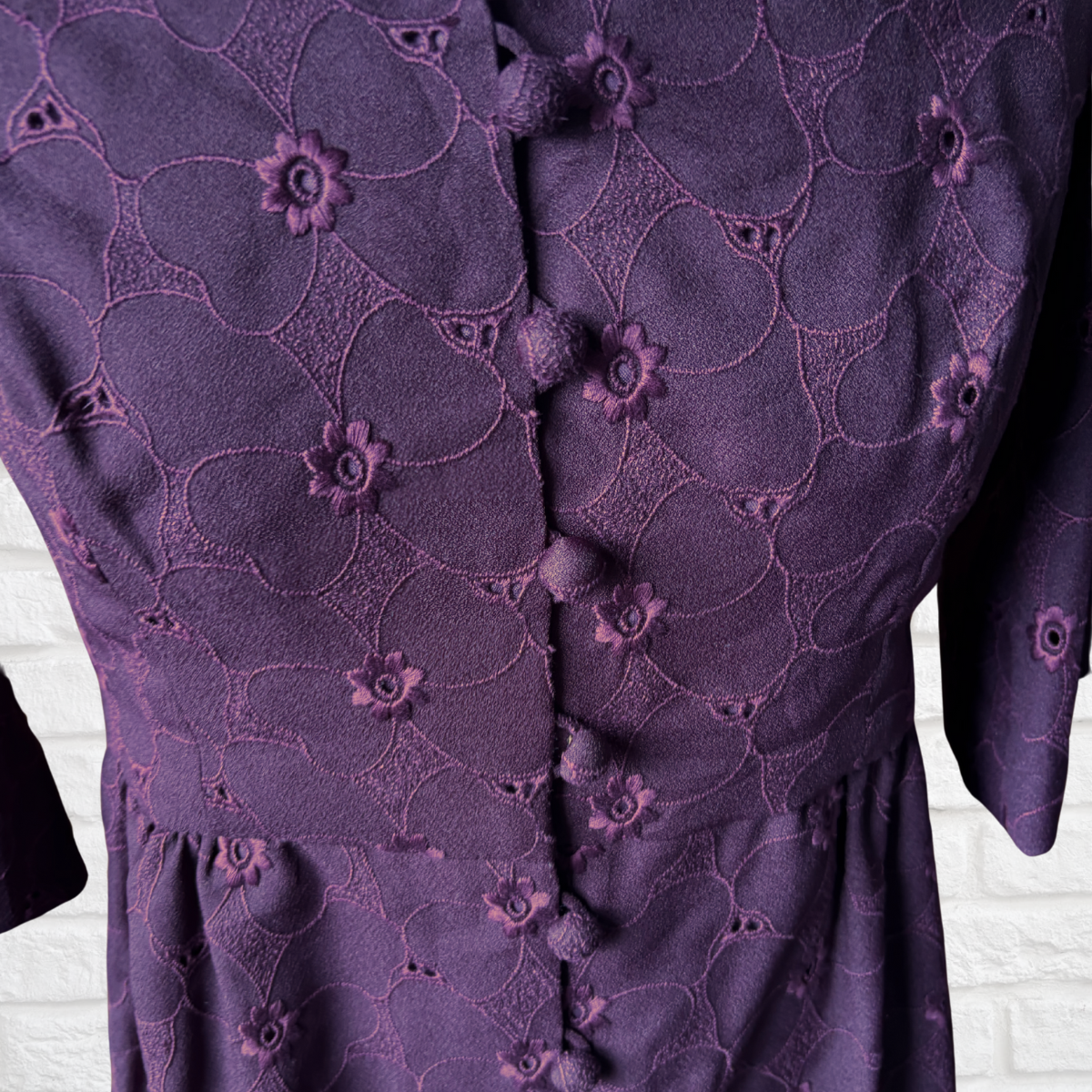 Close-up of a purple dress with floral embroidery on a white brick wall background
