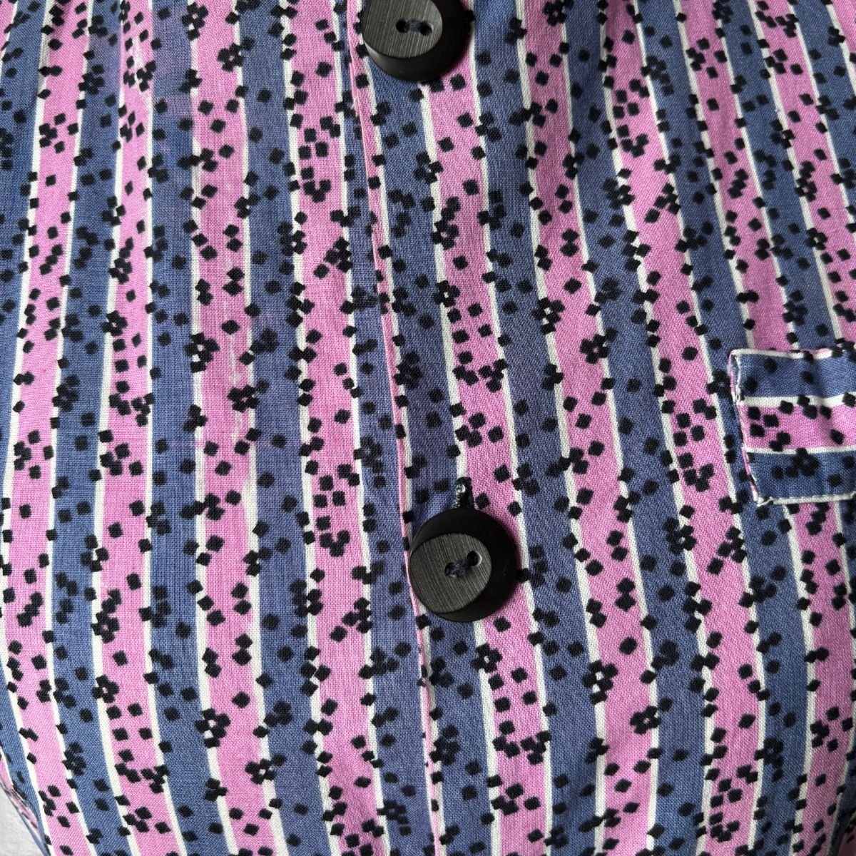 Close-up of a vintage dress with pink and blue striped pattern and black speckles.