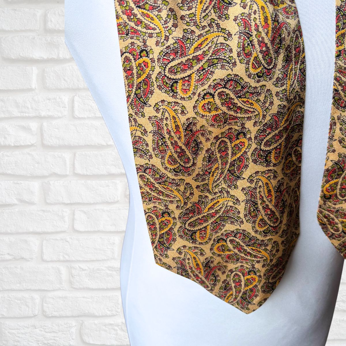 Patterned tie on a mannequin against a white brick wall background