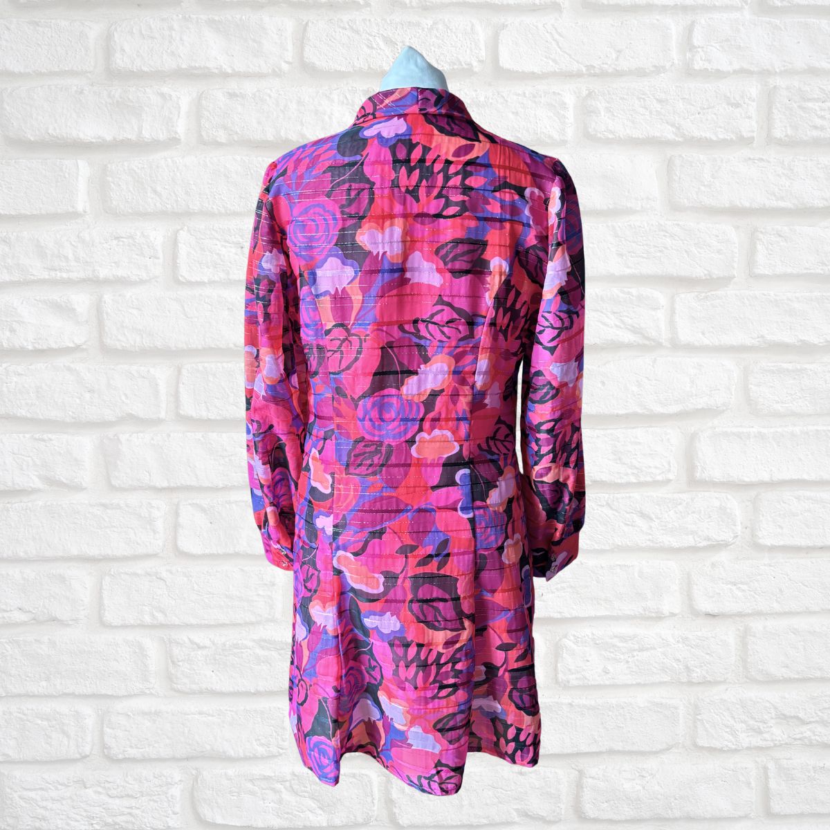 Colorful floral-patterned shirt on a mannequin against a white brick wall background