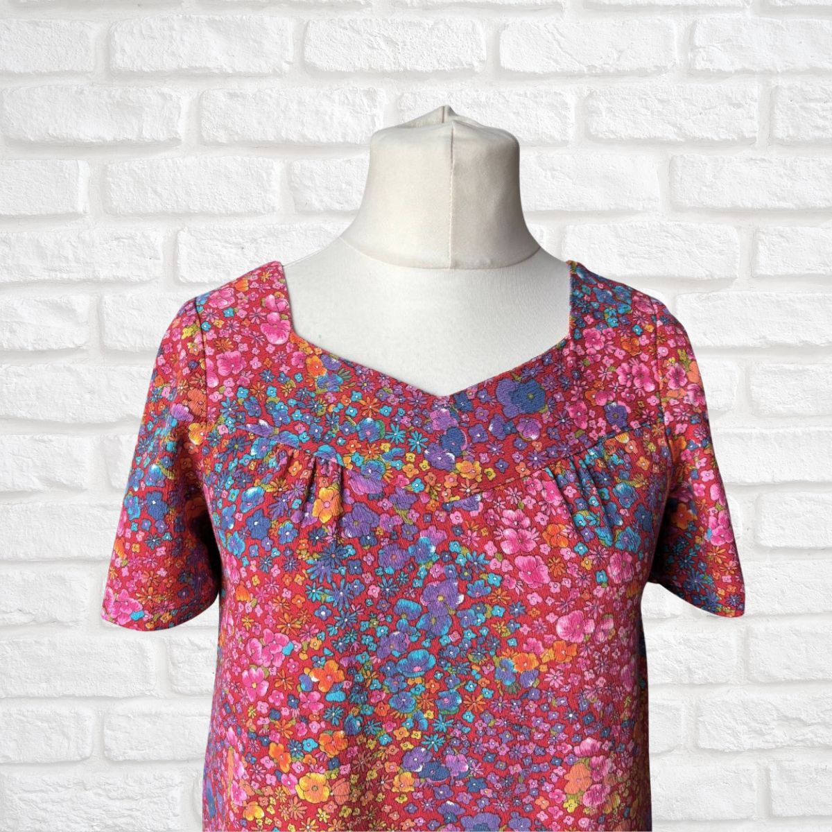 Colorful floral-patterned dress on a mannequin against a white brick wall.