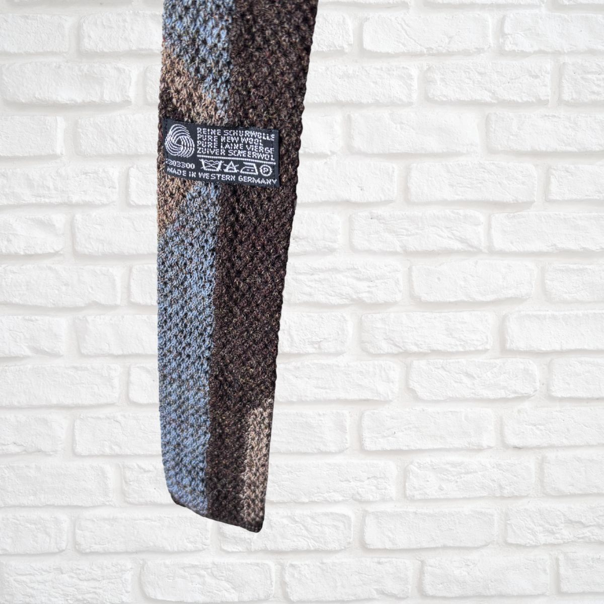 Textured tie with a brand label on a white brick wall background