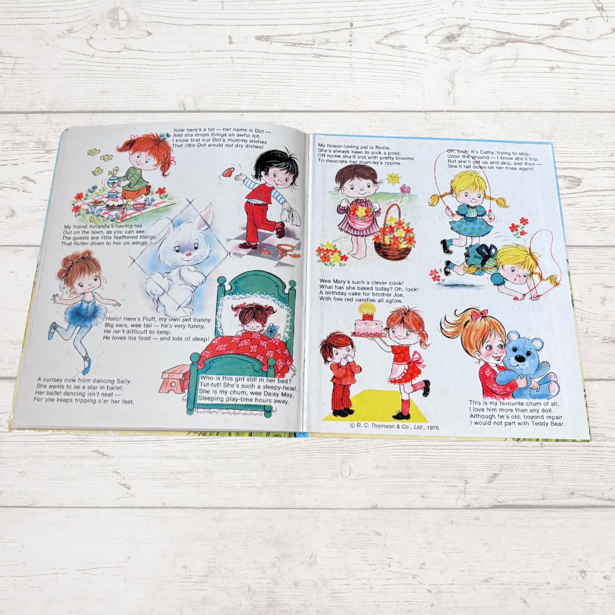An open vintage children's book with colorful cartoon illustrations and printed text, laid flat on a light whitewashed wooden surface.