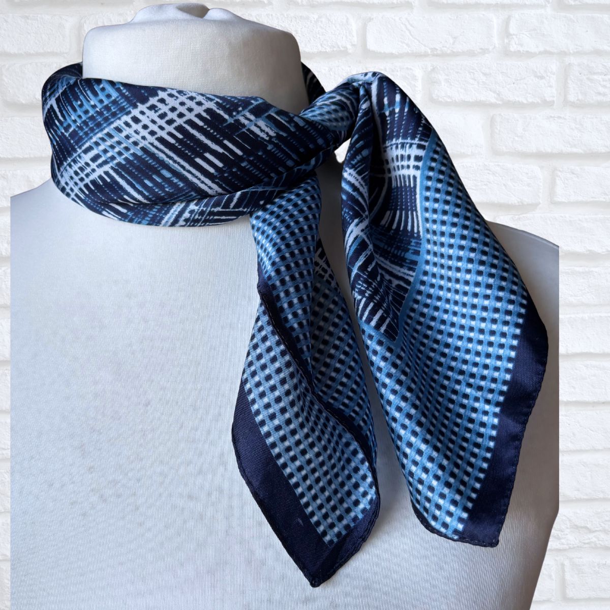 Blue and white patterned scarf on a mannequin against a white brick wall.