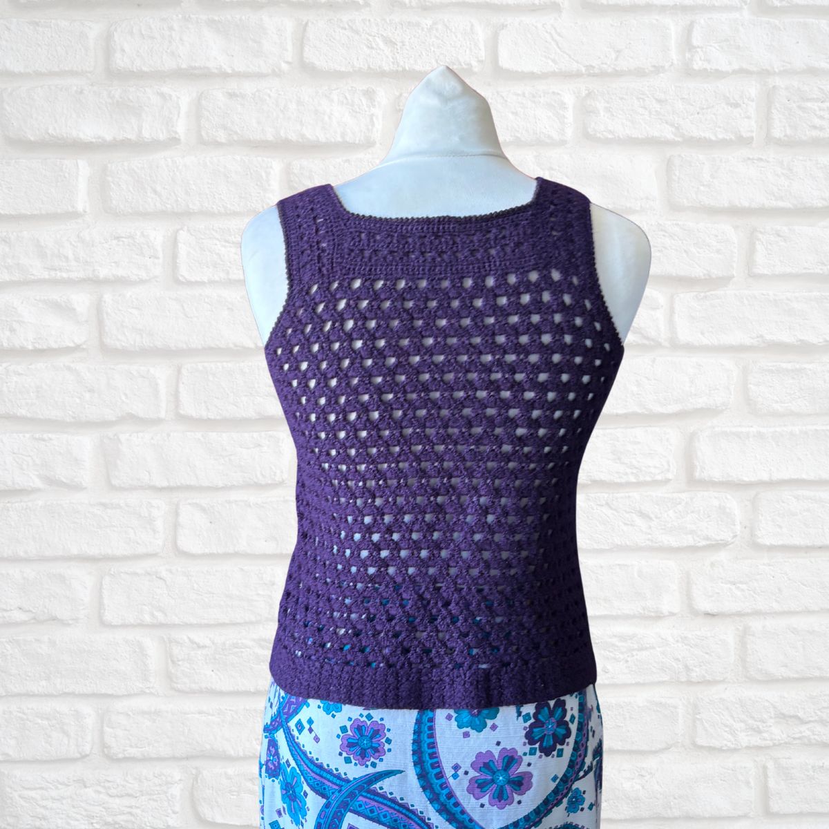 Purple crochet top on a mannequin against a white brick wall background