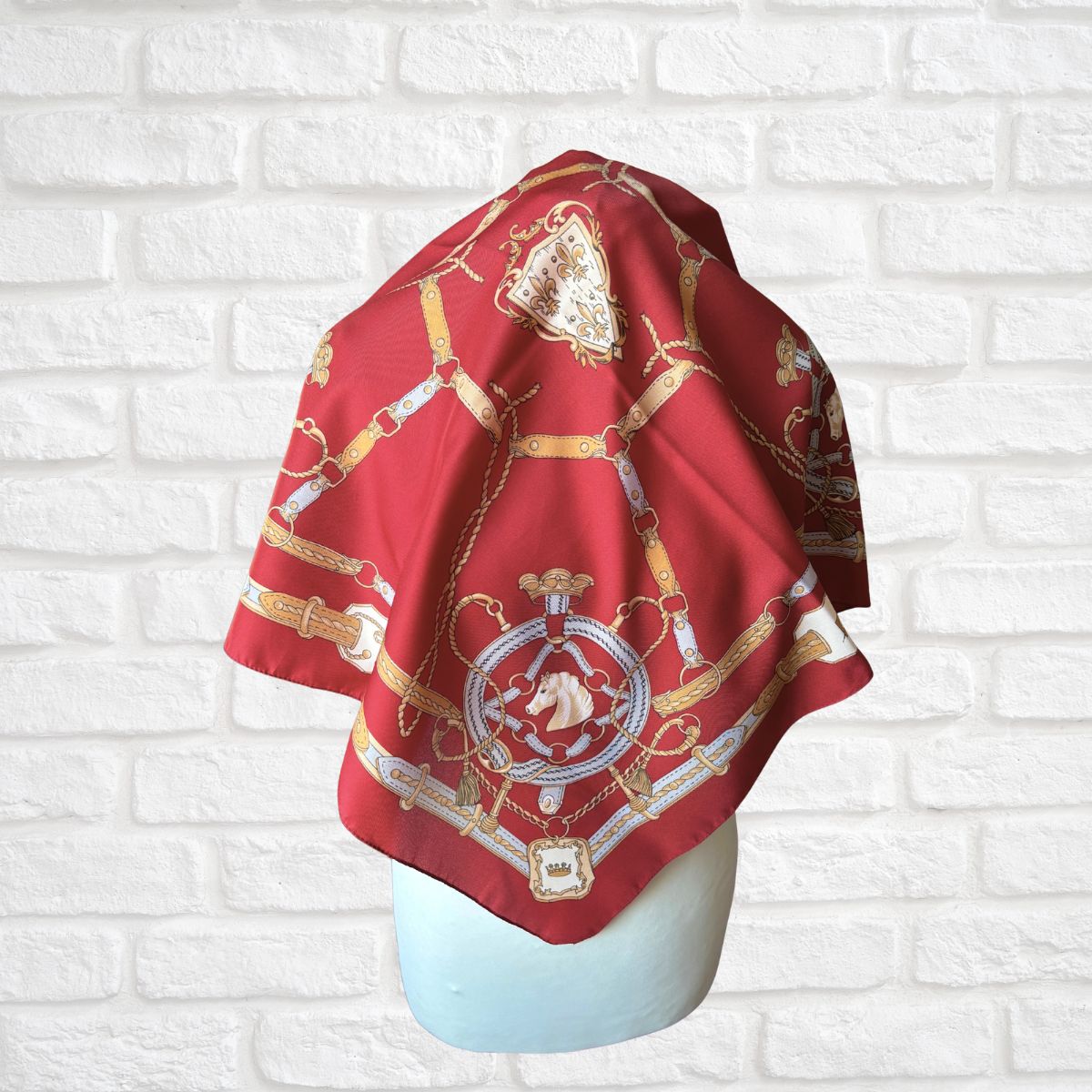 Red scarf with gold and white patterns on a mannequin against a white brick wall.
