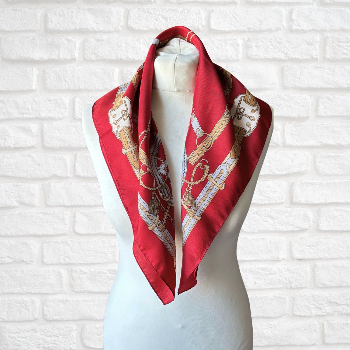 Red scarf with gold patterns on a mannequin against a white brick wall.