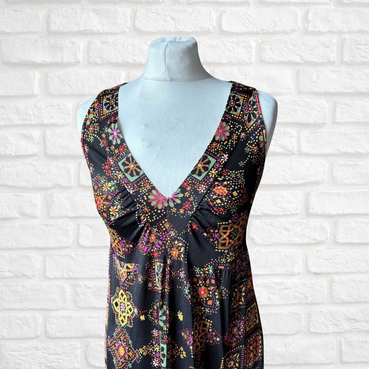 Colorful patterned dress on a mannequin against a white brick wall.