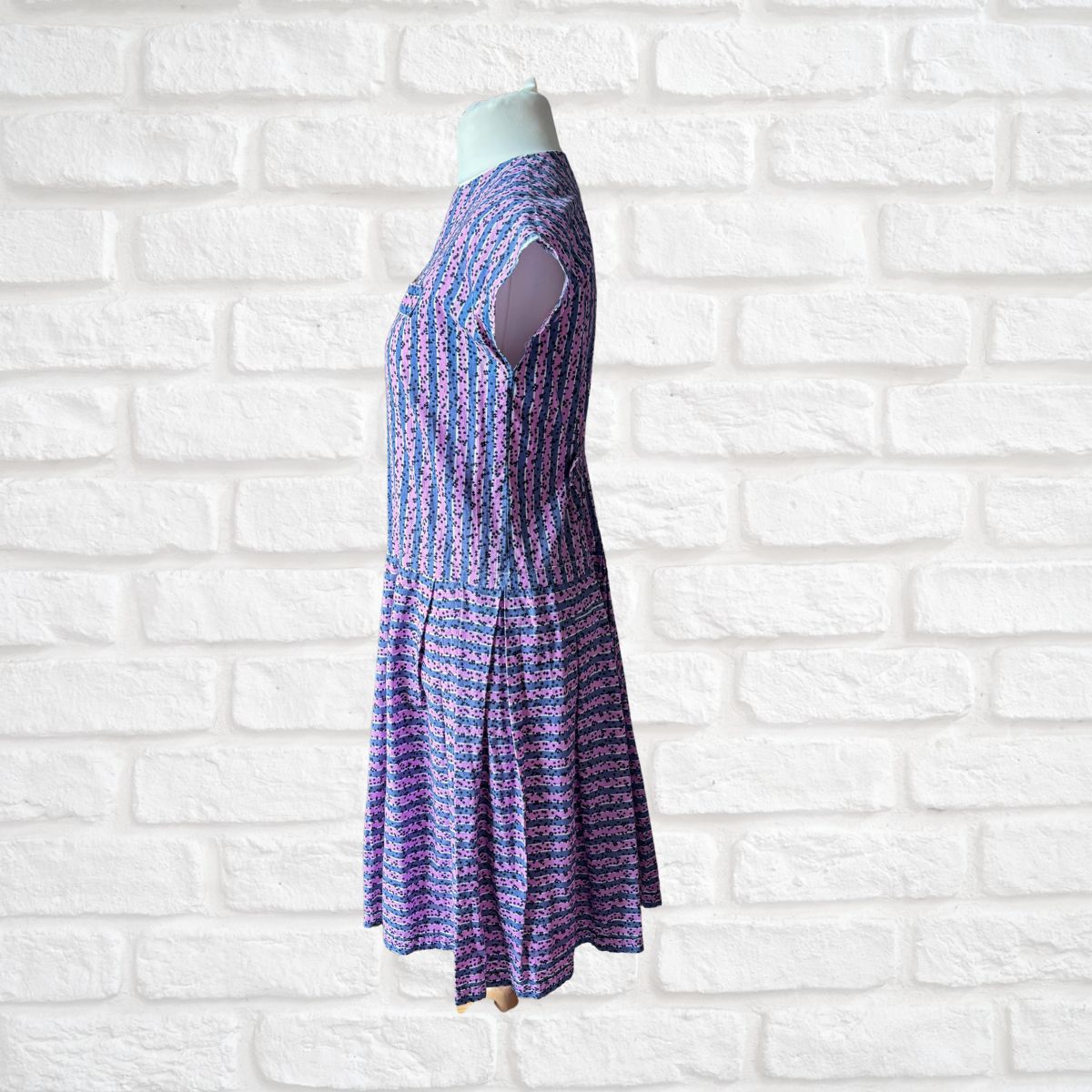 Purple patterned dress on a mannequin against a white brick wall background