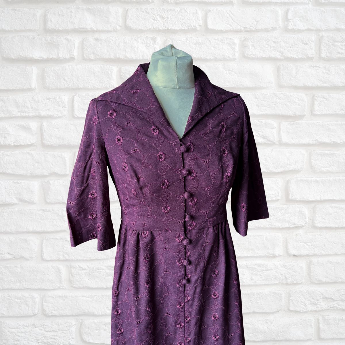Purple dress with floral patterns on a mannequin against a white brick wall background