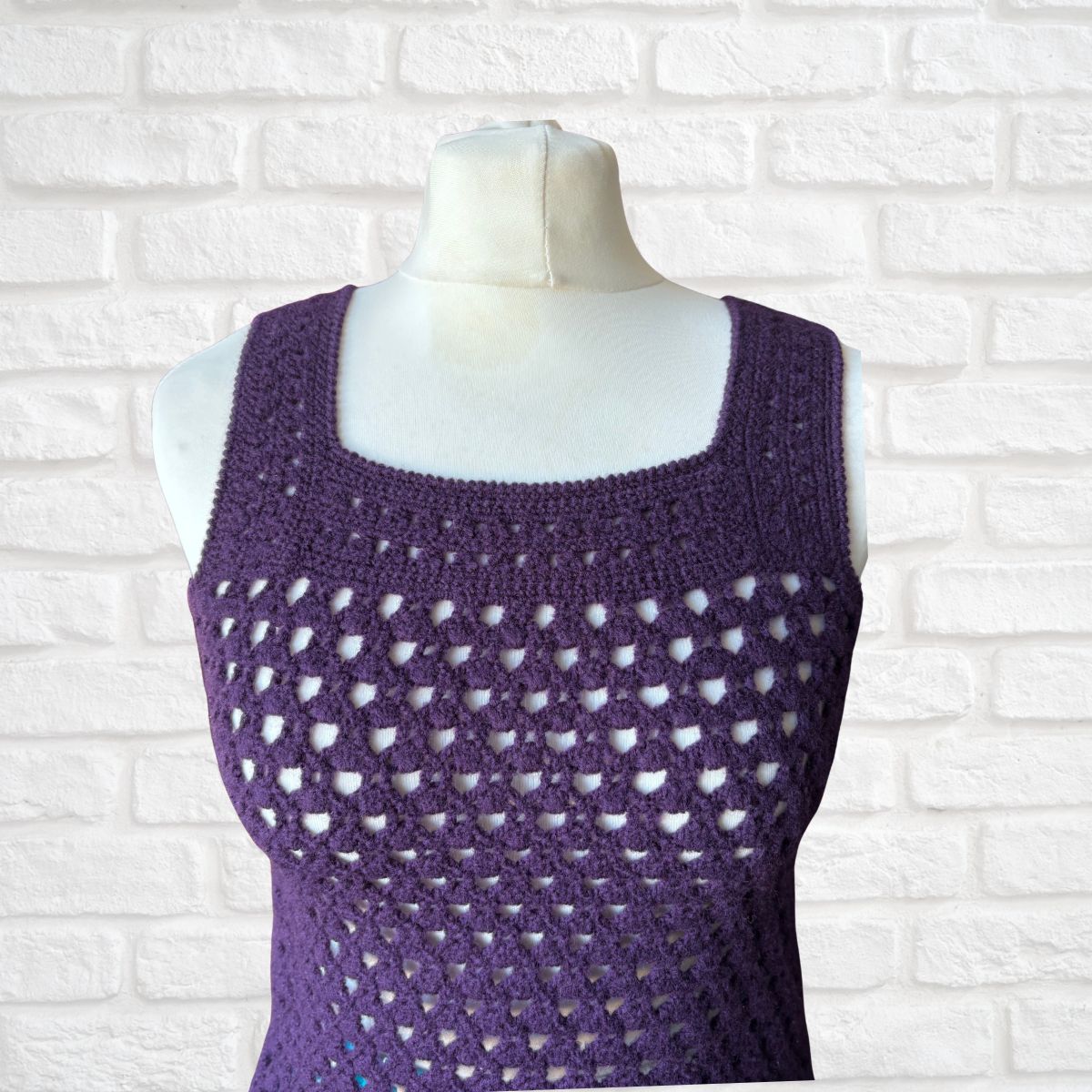 Purple crochet tank top on a mannequin against a white brick wall background