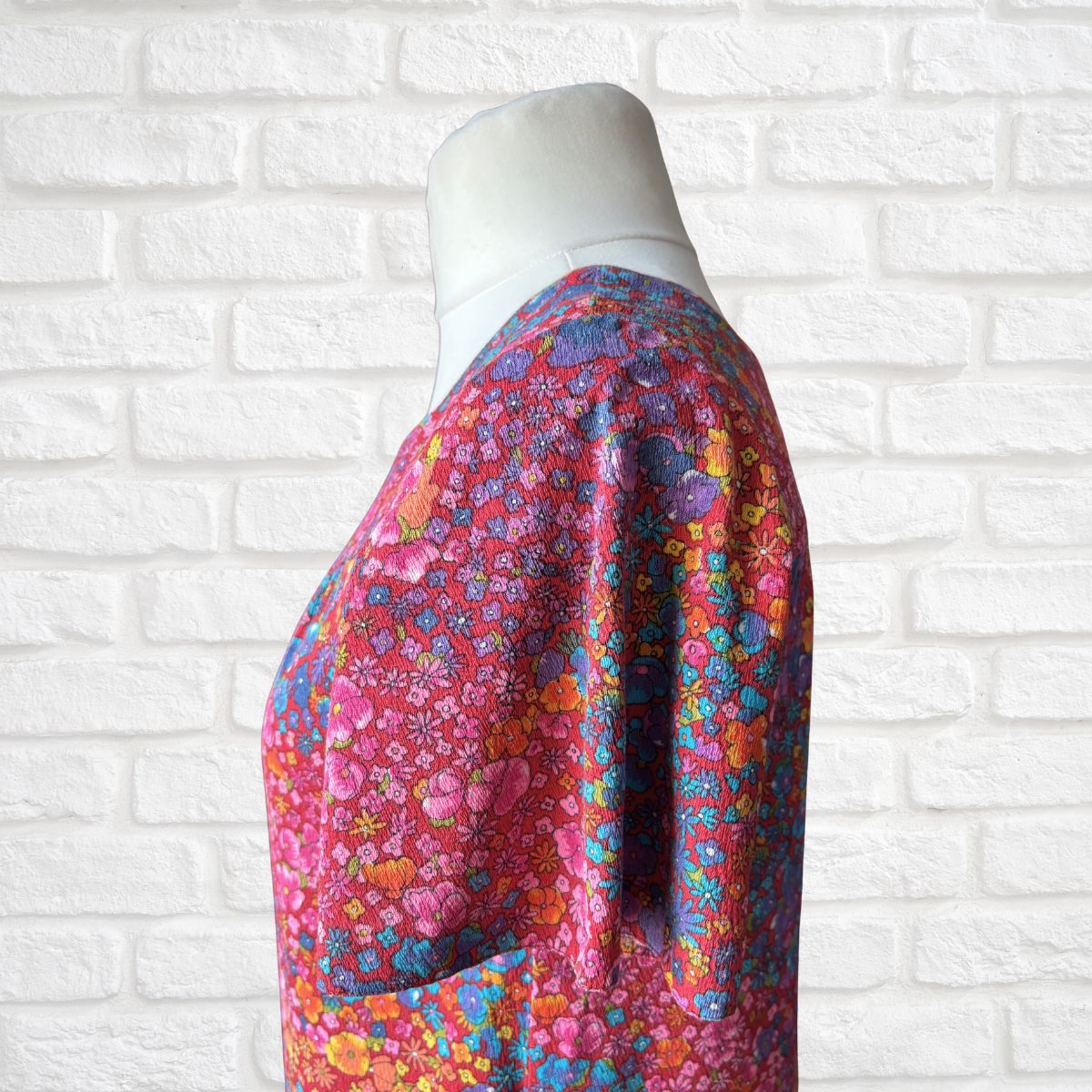 Colorful floral-patterned garment on a mannequin against a white brick wall.