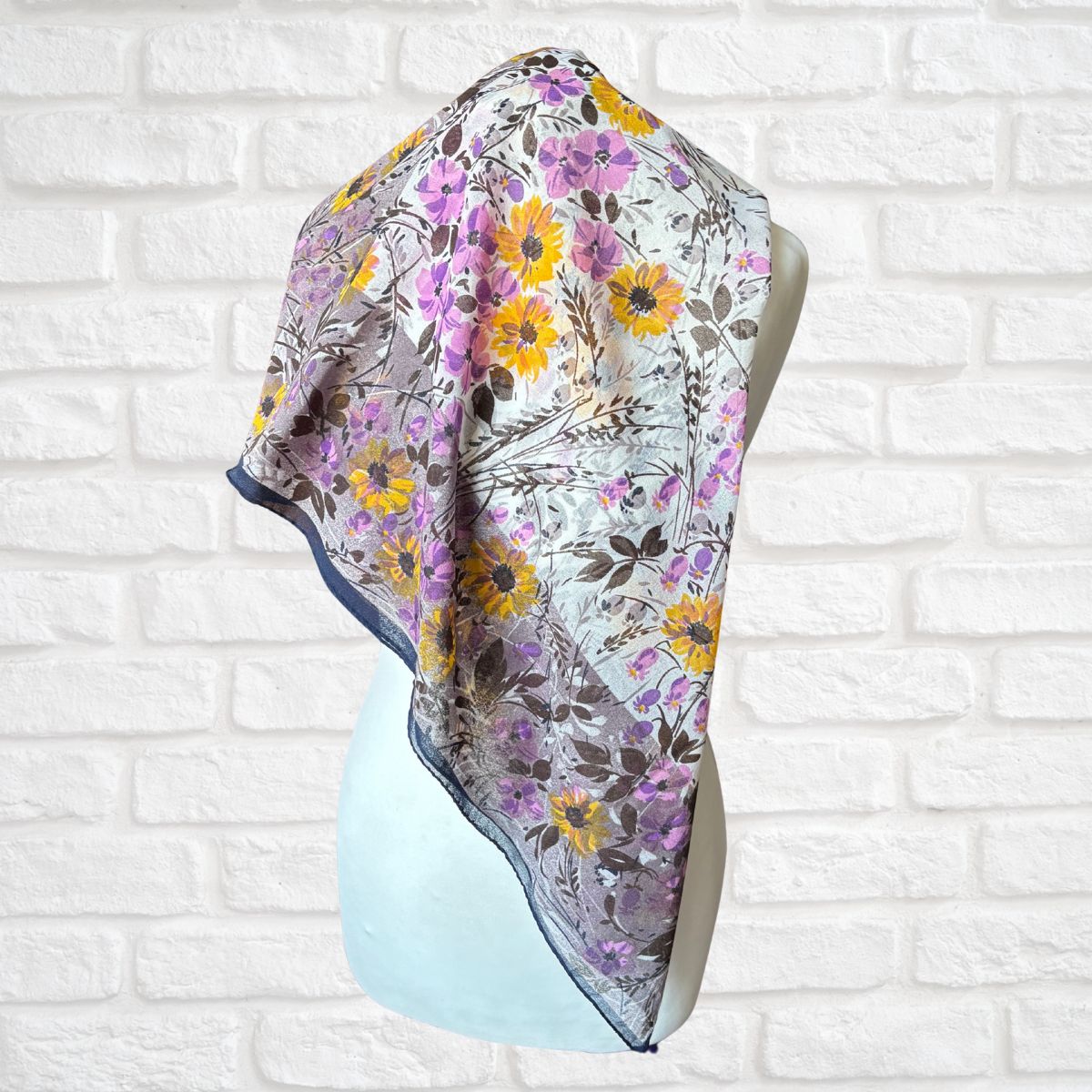 Floral patterned scarf on a mannequin against a white brick wall background