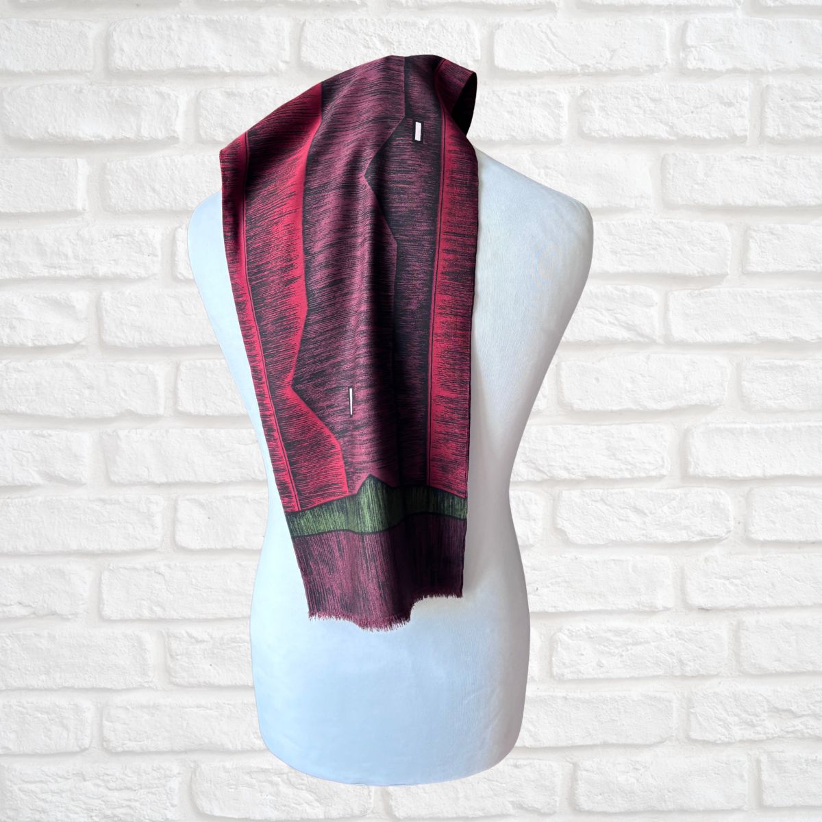 A patterned scarf draped over a white mannequin torso, set against a white brick wall background.