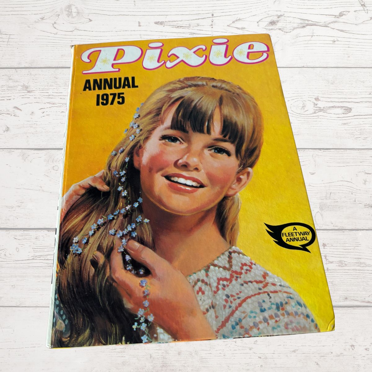 Vintage 'Pixie Annual 1975' book cover with a girl and hand on a wooden surface