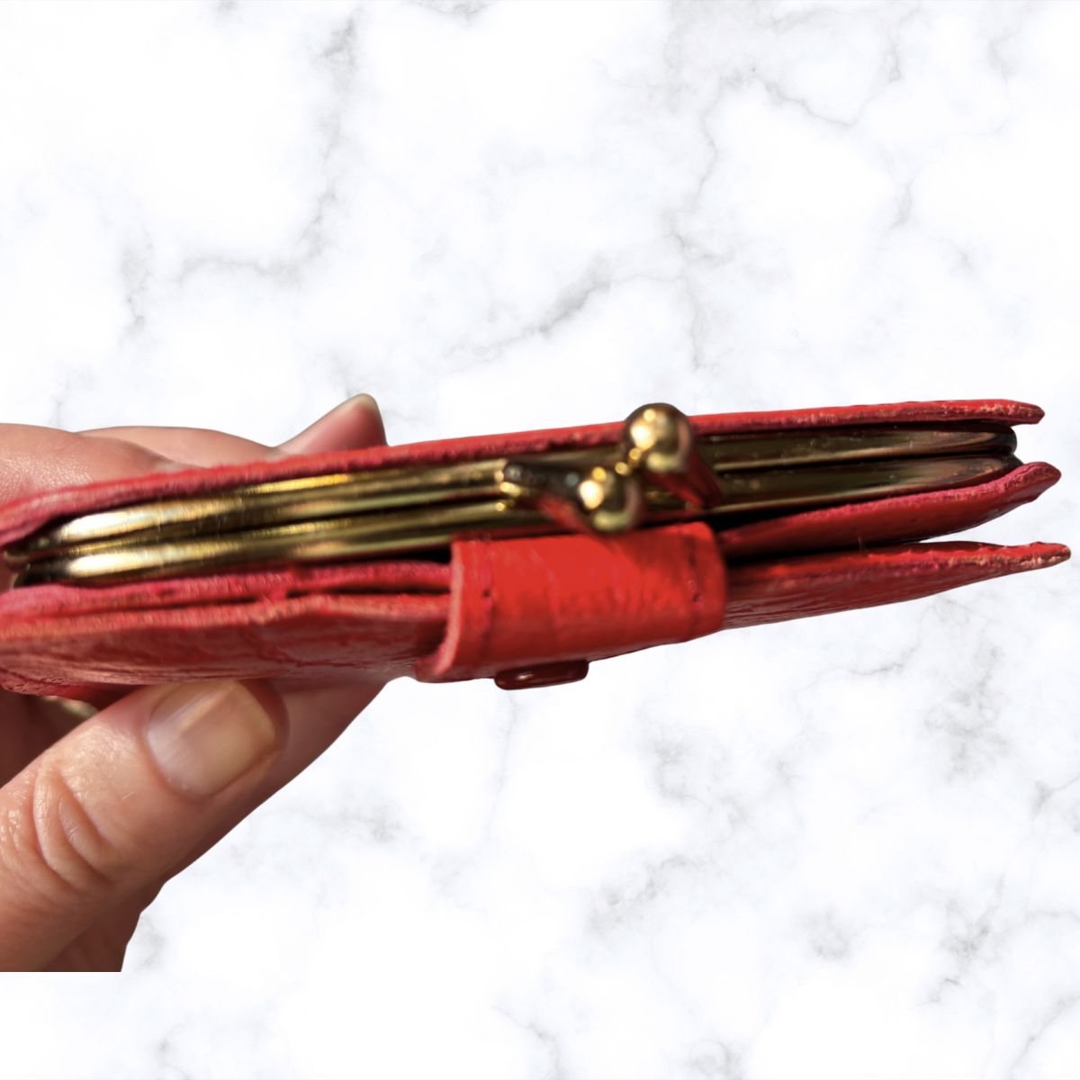Red wallet with gold accents held by a hand against a white background