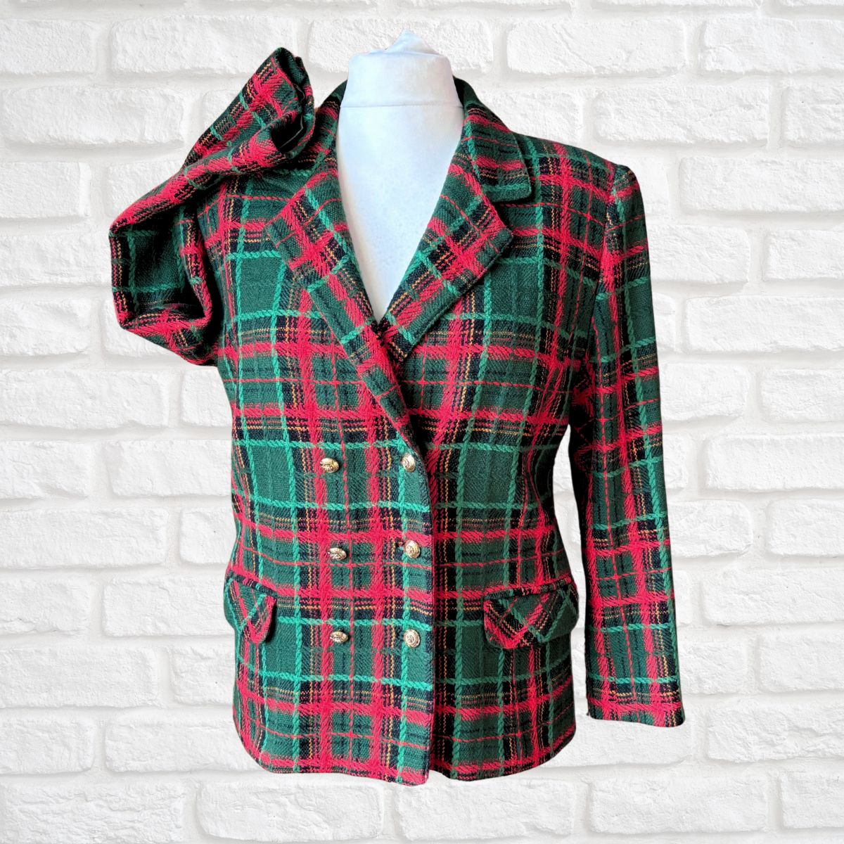 A women's double-breasted plaid blazer jacket in green and red tartan, displayed on a white mannequin torso against a white brick wall background.