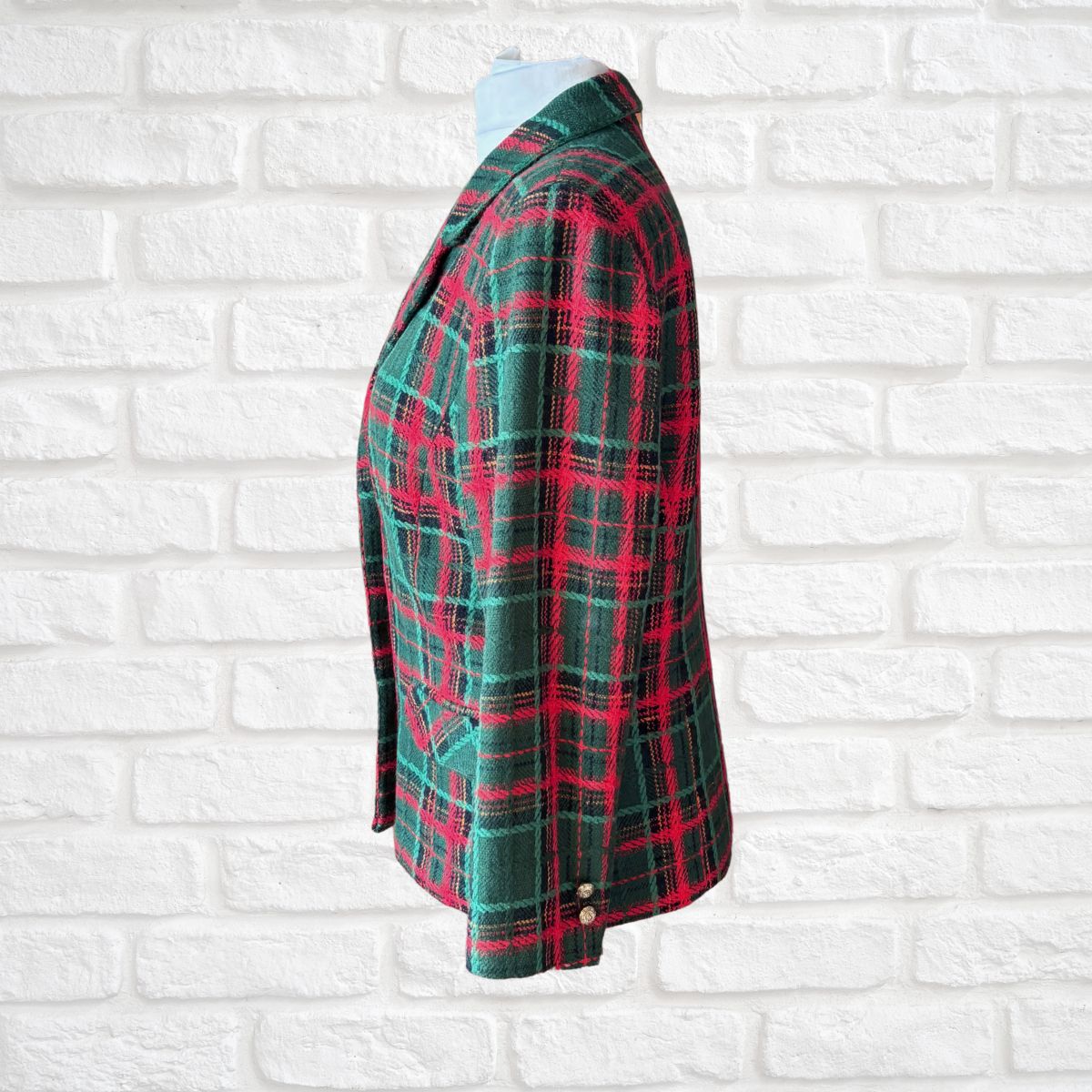 A green and red tartan plaid blazer displayed on a white mannequin torso against a white painted brick wall background.