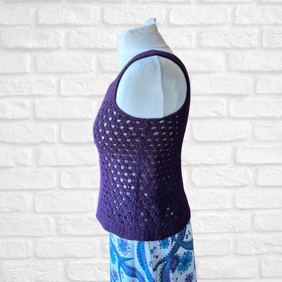 Purple crochet top on a mannequin against a white brick wall background
