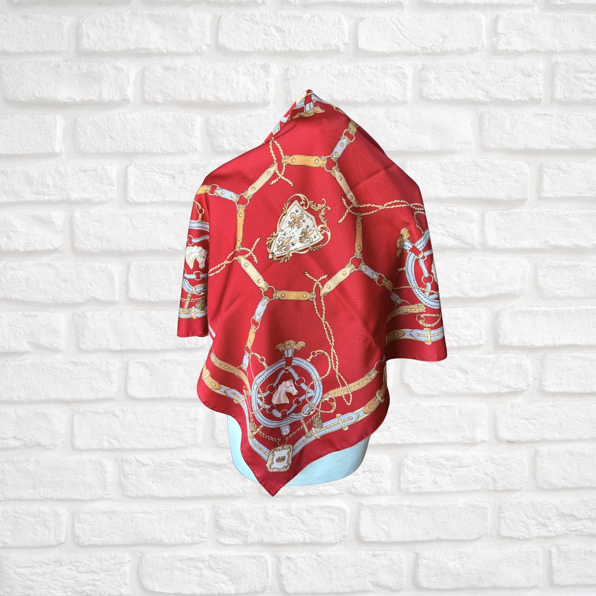 Red scarf with gold and white patterns on a white brick wall background